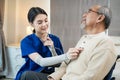 Asian nurse at nursing home taking care of senior man on wheelchair. Young woman therapist doctor measure heart rate by