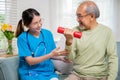 Asian nurse physiotherapist helping senior man in lifting dumbell at retirement home Royalty Free Stock Photo