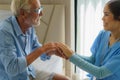 Asian nurse standing on a home bed next to an older man helping hands, care. Elderly patient care and health lifestyle, medical Royalty Free Stock Photo