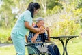 Asian nurse woman help senior man on wheelchair to drink tea in a cup and they stay in the garden with warm light Royalty Free Stock Photo