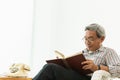 Asian Old man glasses professor sitting on the chair reading textbook Royalty Free Stock Photo