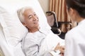 Asian old man lying in bed talking to young female doctor in hospital ward Royalty Free Stock Photo