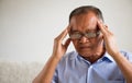 Asian old man sitting on sofa and having a headache at home. Senior healthcare concept Royalty Free Stock Photo