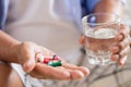 Asian old man taking in pill and another hand holding a glass of clean mineral water. Senior healthcare and medicine concept Royalty Free Stock Photo