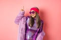 Asian old woman in fashionable glittering dress and purple faux fur coat dancing disco, pointing finger up and having