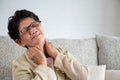 Asian old woman sitting on sofa and having neck pain, backache at home. Senior healthcare concept Royalty Free Stock Photo