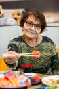 Asian old woman tourist face camera smiling fork in hand showing local food or Japanese food. A woman aged and will show you sus