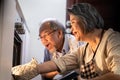 Asian older grandparents making pizza at home. Senior woman open the oven and bring the foods out from machine. Elder man looking Royalty Free Stock Photo