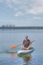 Asian older man on sup board on calm lake.