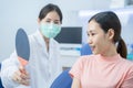 Asian orthodontist hold the mirror to let young girl patient check her braces after adjusting the wire. Woman look to mirror, open Royalty Free Stock Photo