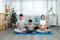 Asian parent and son sitting in yoga meditation pose in living room. son follows