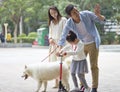 Asian parents & daughter playing scooter while walking dog in garden