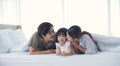 Asian Parents lying on bed under blanket and kissing their little daughter on both cheeks Royalty Free Stock Photo