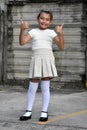 Pretty Philippina Child With Thumbs Up Wearing Skirt Near Wall