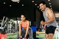 Asian personal trainer coaching a bodybuilding woman to perform crossfit battle ropes exercise in the fitness gym