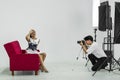 An Asian photographer is photographing a model posing on a red sofa for advertising in a magazine Royalty Free Stock Photo