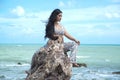 Asian plus size fat and overweight woman in a white dresses sitting on rock on the beach. Royalty Free Stock Photo