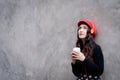 Asian portrait woman with red hat and black clothes has holding a cup of coffee with happiness and the grey stone wallpaper Royalty Free Stock Photo