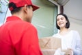 Asian Postman delivery delivering package of goods to young Caucasian cute customer girl at home. Beautiful woman receive boxes fr