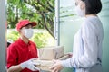 Asian postman, deliveryman wearing mask carry small box deliver to customer in front of door at home. Man wearing mask prevent cov Royalty Free Stock Photo
