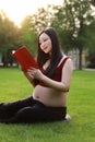 Asian pregnant woman Chinese read red cover book sit on grass lawn in nature outdoor sunshine sunset sunrise day enjoy peaceful Royalty Free Stock Photo