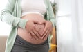 Asian pregnant woman hands making heart gesture on belly at home. Pregnancy, maternity, preparation and expectation concept Royalty Free Stock Photo