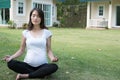 asian pregnant woman practicing yoga while sitting in lotus position on green grass in front of her house. meditating on Royalty Free Stock Photo