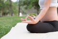 asian pregnant woman practicing yoga while sitting in lotus position on green grass in public park. meditating on maternity. Royalty Free Stock Photo