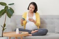 Asian pregnant woman using mobile phone searching information and reading medicine label and prescription medications