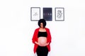 Asian pregnant woman wearing red suit, standing, looking and touching or holding her belly on white wall background and copy space Royalty Free Stock Photo