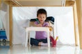 Asian preschool boy drawing in paper while lying in a blanket fort in living room at home for perfect hideout away from their