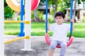 Asian preschool little child boy sitting on red swings  lonely or sad gestures unhappy. A scared little child is 2 years old. Royalty Free Stock Photo