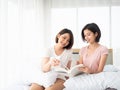 Asian pretty two girl open book with smile and reading fiction together hobby lifestyle in the weekend on white bed with blanket Royalty Free Stock Photo