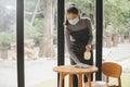 Asian pretty waitress staff wearing protection face mask in apron cleaning table with disinfectant spray for protect infection cor Royalty Free Stock Photo