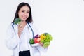 Asian pretty woman doctor, nutritionist holding and showing many fresh vegetables and fruit with high vitamin C