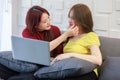 Asian pretty young female lesbian lover sitting smiling on cozy sofa with couple partner using laptop computer browsing surfing Royalty Free Stock Photo