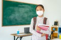 Asian primary students girl with backpack and books wearing masks to prevent the outbreak of Covid 19 in classroom while back to Royalty Free Stock Photo