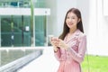 Asian professional  business woman with long hair  smiling in front of the office while using a smartphone in her hand to work Royalty Free Stock Photo