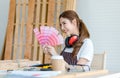 Asian professional cheerful female carpenter worker staff in apron with earphones sitting smiling showing colorful color chart