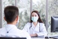 Asian professional female doctor wears medical coat and face mask while examines and talks with a man patient in examination room