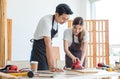 Asian professional male carpenter in apron complimenting showing thumb up to female lover worker using polishing machine rubbing