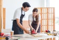 Asian professional male carpenter in apron complimenting showing thumb up to female lover worker using polishing machine rubbing