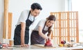 Asian professional male carpenter in apron complimenting showing thumb up to female lover worker using polishing machine rubbing