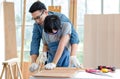 Asian professional male carpenter woodworker engineer dad in jeans outfit with safety gloves goggles helping teaching young boy Royalty Free Stock Photo