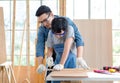 Asian professional male carpenter woodworker engineer dad in jeans outfit with safety gloves goggles helping teaching young boy Royalty Free Stock Photo