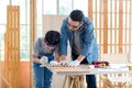 Asian professional male carpenter woodworker engineer dad in jeans outfit with safety gloves goggles helping teaching young boy Royalty Free Stock Photo