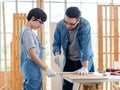 Asian professional male carpenter woodworker engineer dad in jeans outfit with safety gloves goggles helping teaching young boy Royalty Free Stock Photo