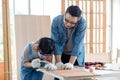 Asian professional male carpenter woodworker engineer dad in jeans outfit with safety gloves goggles helping teaching young boy Royalty Free Stock Photo