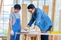 Asian professional male carpenter woodworker engineer dad in jeans outfit with safety gloves goggles helping teaching young boy Royalty Free Stock Photo