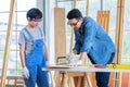 Asian professional male carpenter woodworker engineer dad in jeans outfit with safety gloves goggles helping teaching young boy Royalty Free Stock Photo